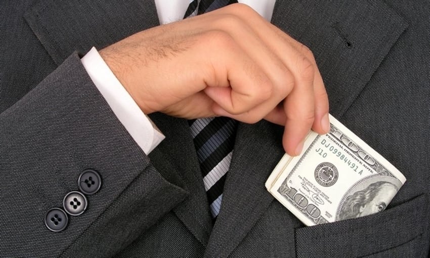 Businessman slipping hundred dollar bills into breastpocket of expensive suit