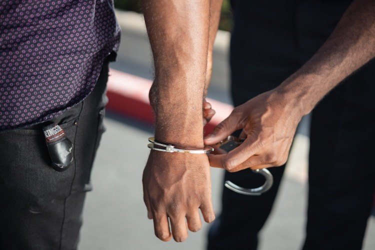 Officer handcuffing man in black jeans and purple shirt outdoors