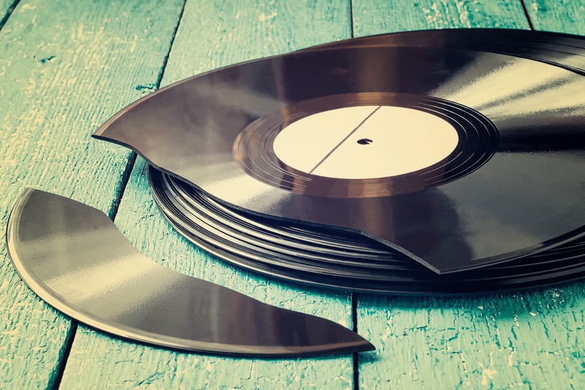 Stack of records on a painted deck, with the top record snapped into two pieces