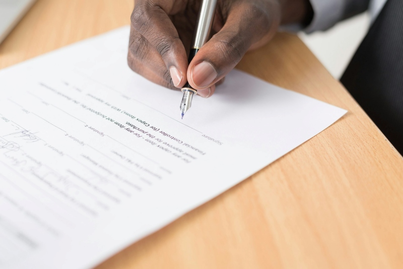 Close-up view of hand signing contract on light wooden desk