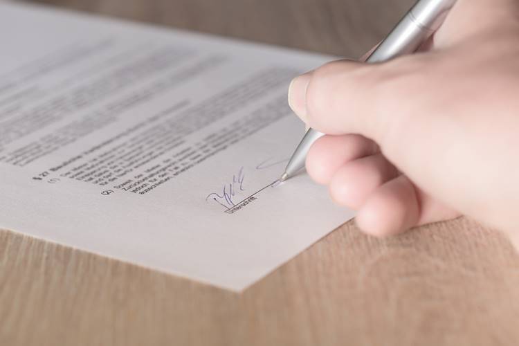 Close-up view of hand signing contract on light wooden desk
