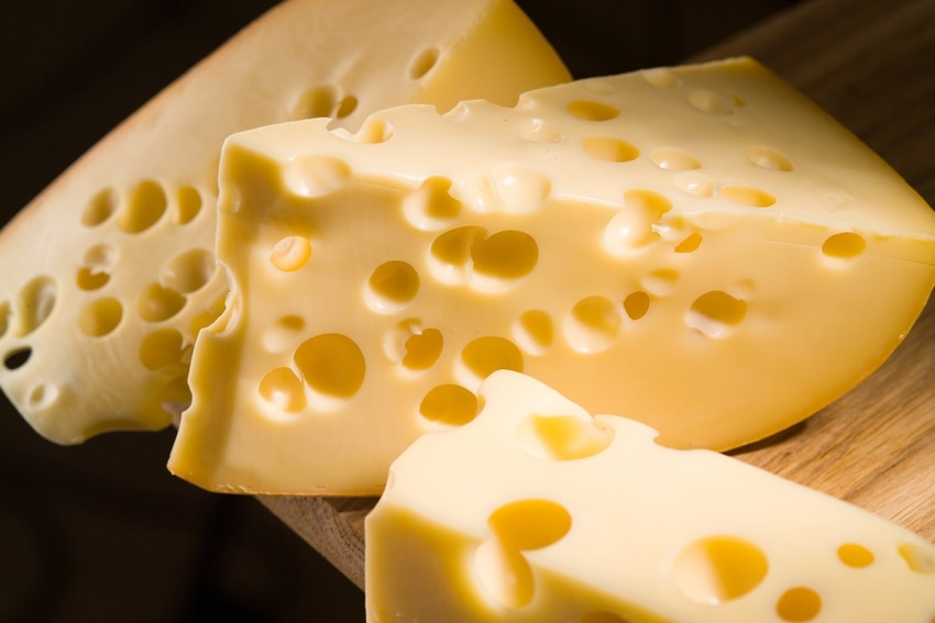 Slices of swiss cheese on wooden chopping block over black background