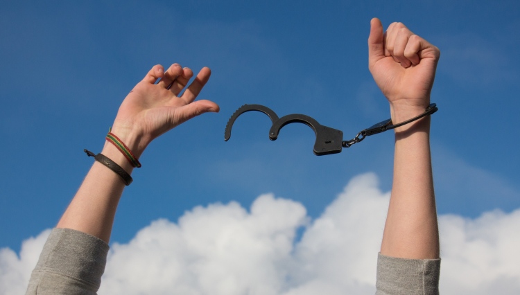 Arms raised to cloudy outdoor sky with one wrist handcuffed and one freed