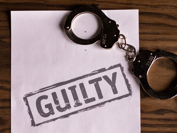 Closed handcuffs and paper stamped with "GUILTY" in black on wooden desk