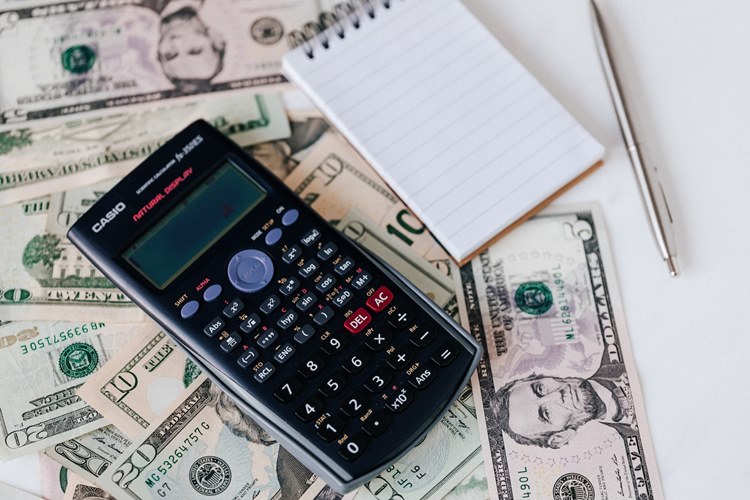 Cash spread across white table with calculator, notepad and pen