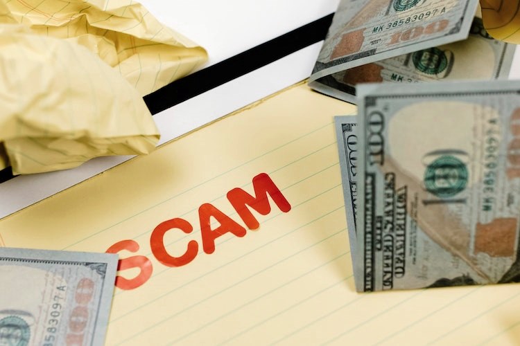 'SCAM' stamped in red letters on memo pad beside hundred dollar bills