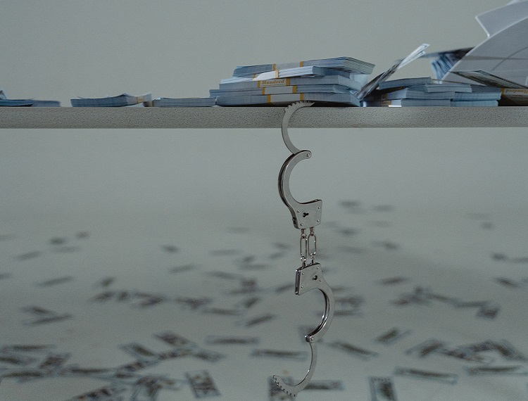 Handcuffs and piles of cash on white table with cash strewn on floor below