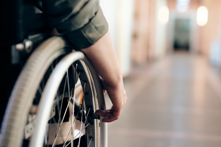 Close-up of wheelchair wheel and hand of user facing empty hallway
