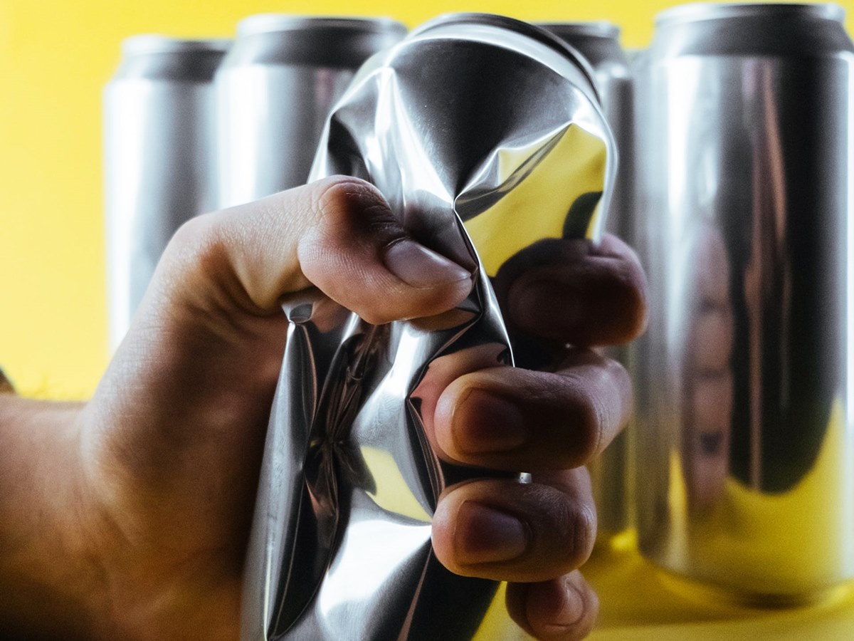 Hand crushing aluminum beer can with several empty cans in background