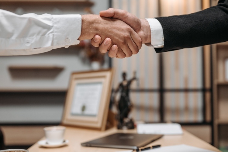 Close-up view of handshake between lawyer in pantsuit and client in white dress shirt over wooden desk