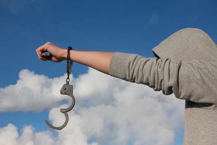 Teenager outdoors in gray hoodie extending arm with handcuff on one wrist