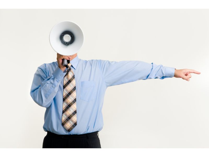 Government official in men's dress shirt and tie pointing angrily while shouting through bullhorn