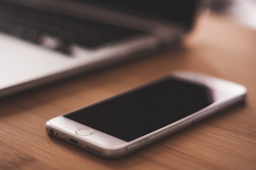 White iPhone sitting beside laptop on wooden desk